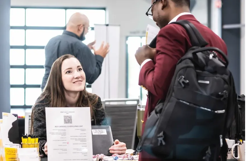 Woman sitting at table looks up at person during career fair.